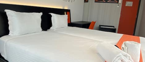 A hotel room with a large bed, white bedding, an orange throw, and a cityscape mural on the wall.