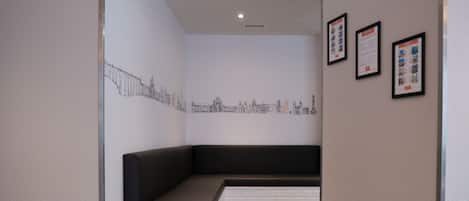 A modern interior with a black cushioned bench, white brick accents, and a cityscape mural on the wall.