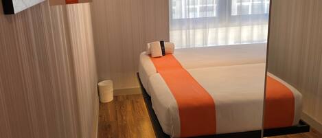 Ein modernes Hotelzimmer mit Bett, Nachttisch, Spiegel und einem Fenster mit Vorhängen.