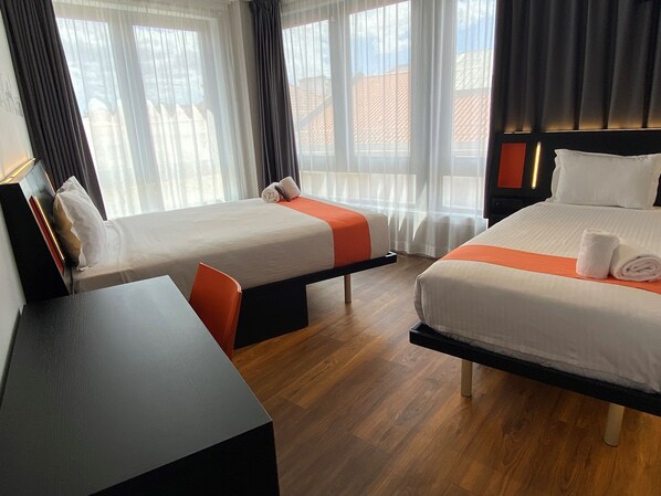 A hotel room with two beds, a desk, and a view of the outside.