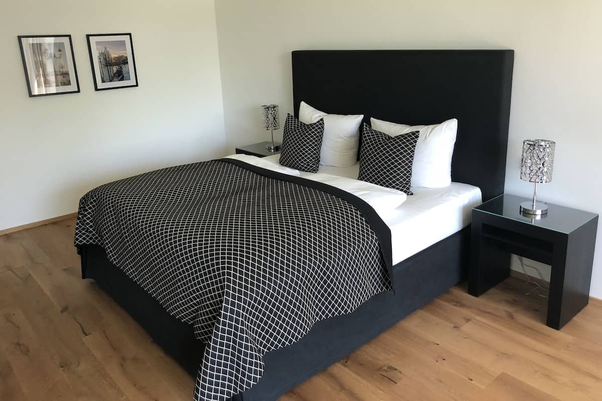 Quarto moderno com colcha quadricula preta e branca, cabeceira preta e mesa de cabeceira com luminária.