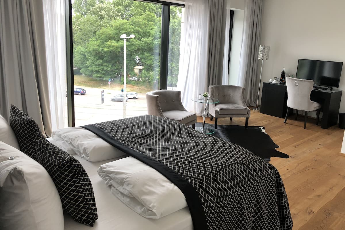 Quarto de hotel moderno com uma cama grande, dois poltronas, uma mesa pequena, uma escrivaninha com televisão e vista para o exterior.