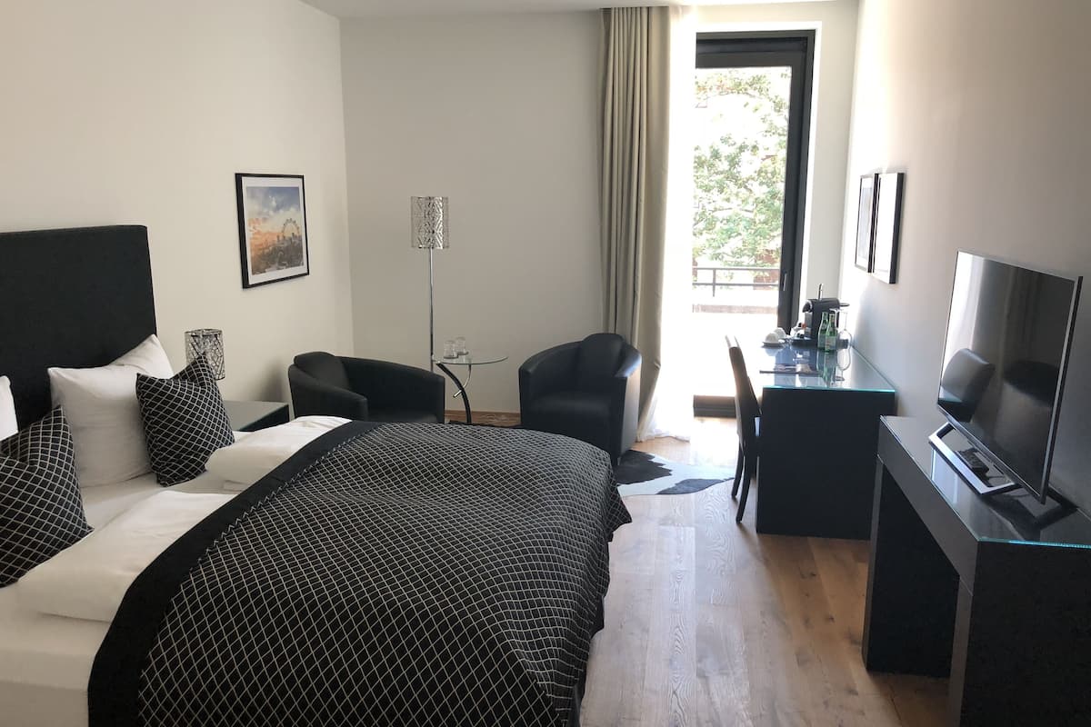 Quarto de hotel com cama, escrivaninha, cadeira, televisão e janela com cortinas.