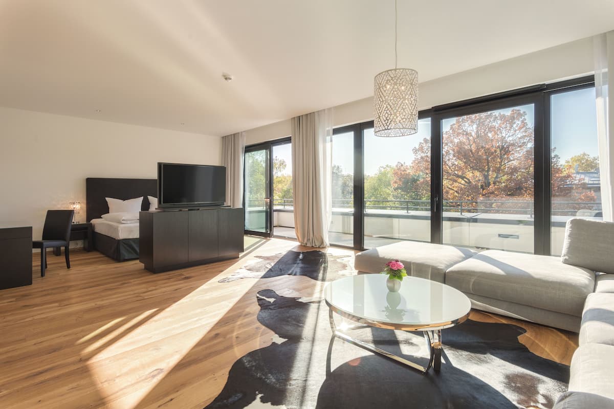 Uma sala de estar moderna com sofá, mesa de centro, televisão e uma janela grande com vista para árvores.