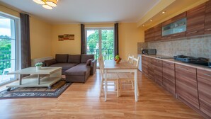 A modern kitchen with wooden cabinets, a dining table, and a sofa in a living area with a view of greenery outside. - RentPlanet - Apartament Mickiewicza (Szklarska Poreba)