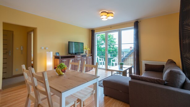 A living room with a wooden dining table, a sofa, and a TV. - RentPlanet - Apartament Mickiewicza (Szklarska Poreba)