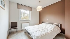 Une chambre à coucher avec un lit, une chaise, une fenêtre et un luminaire au plafond.