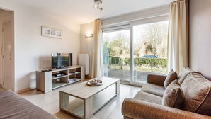 Un salon moderne comprenant un canapé, une table basse, un téléviseur et une porte-fenêtre coulissante donnant sur un balcon.