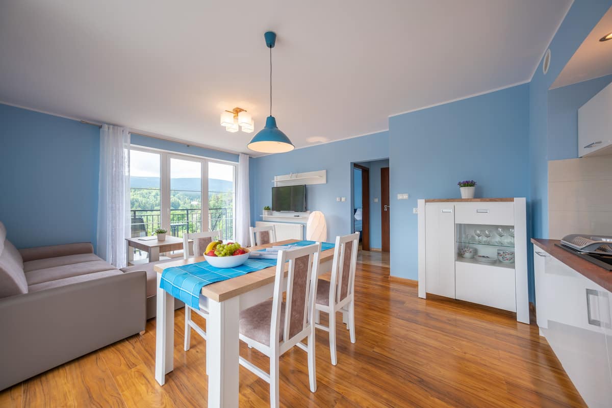 Una cocina moderna con armarios blancos, una mesa de comedor con sillas y una lámpara colgante azul.