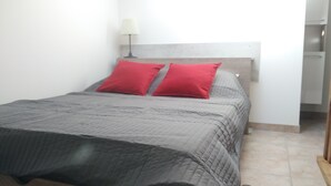 Una cama con colcha gris y dos almohadas rojas, una lámpara de noche y un cabecero de madera.