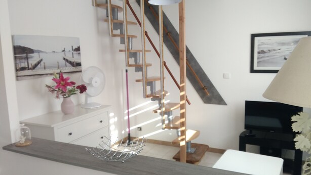Una sala de estar moderna con una escalera, un aparador blanco, un ventilador y un televisor.