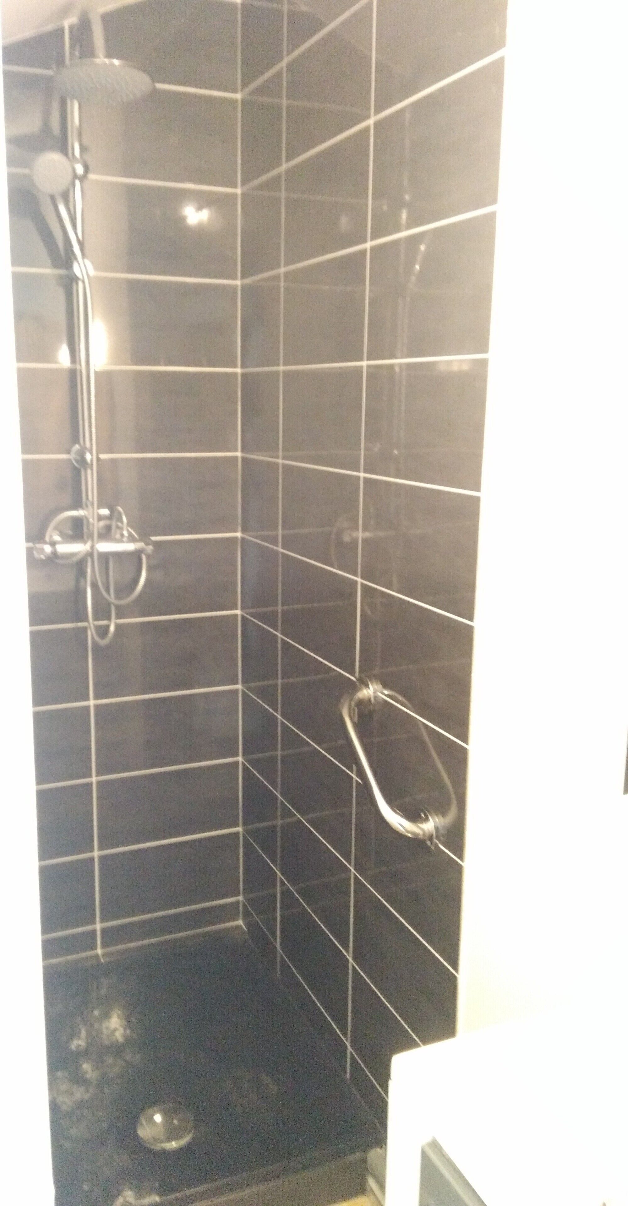 Eine kleine, geflieste Duschkabine mit Handbrause und Duschwand.