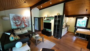 A modern living room with a sofa, coffee table, and a TV. There is a kitchen area with a fridge and a dining table. - Feriendorf Waldbrunn (Waldbrunn)