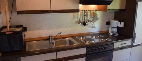 A compact kitchen with a sink, stove, and oven, featuring wooden cabinets and a coffee maker.