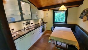 A compact kitchen with a wooden ceiling, a dining table with a bench, and a window with a view of greenery. - Feriendorf Waldbrunn (Waldbrunn)
