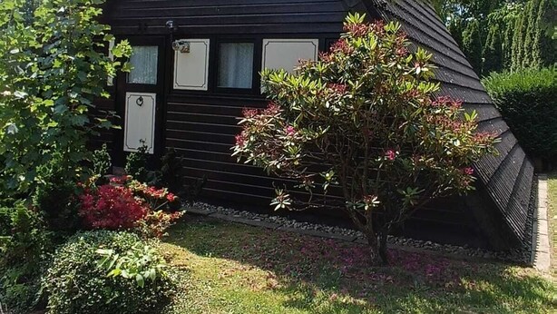 A black wooden house with a triangular roof and a large window. - Feriendorf Waldbrunn (Waldbrunn)