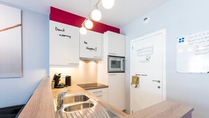 A modern kitchen with a wooden countertop, stainless steel sink, and a microwave. There are cabinets with motivational phrases and a whiteboard with writing. - Jersey 201 (Koksijde)