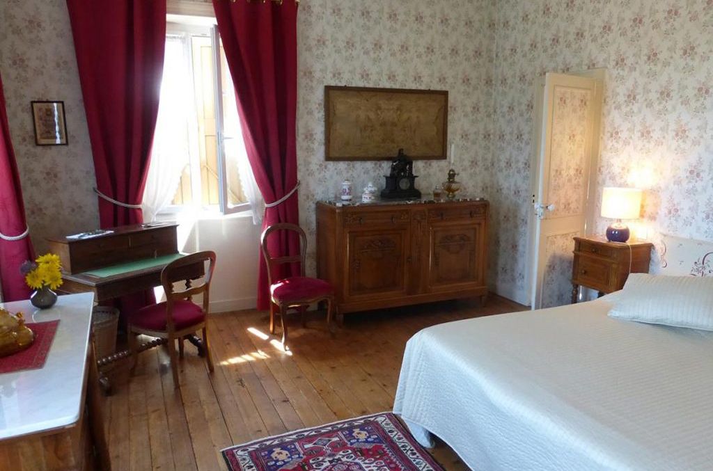 Une chambre à coucher comprenant un lit, une commode en bois, un bureau avec une chaise et une fenêtre avec des rideaux.