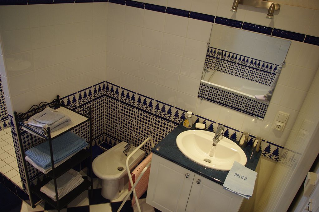 A bathroom with a white sink, a mirror above it, and a toilet. There is a shelf with towels and a rack with folded towels.