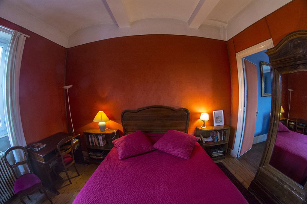 A room with a large bed, two bedside tables with lamps, a wooden desk, and a chair.