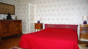 Een slaapkamer met een rood beddegoed, houten meubels en bloemenbehang.