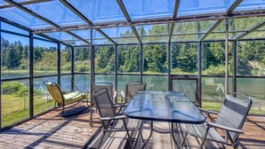 Una terrazza vetrata con tavolo e sedie, vista su un lago e una foresta.