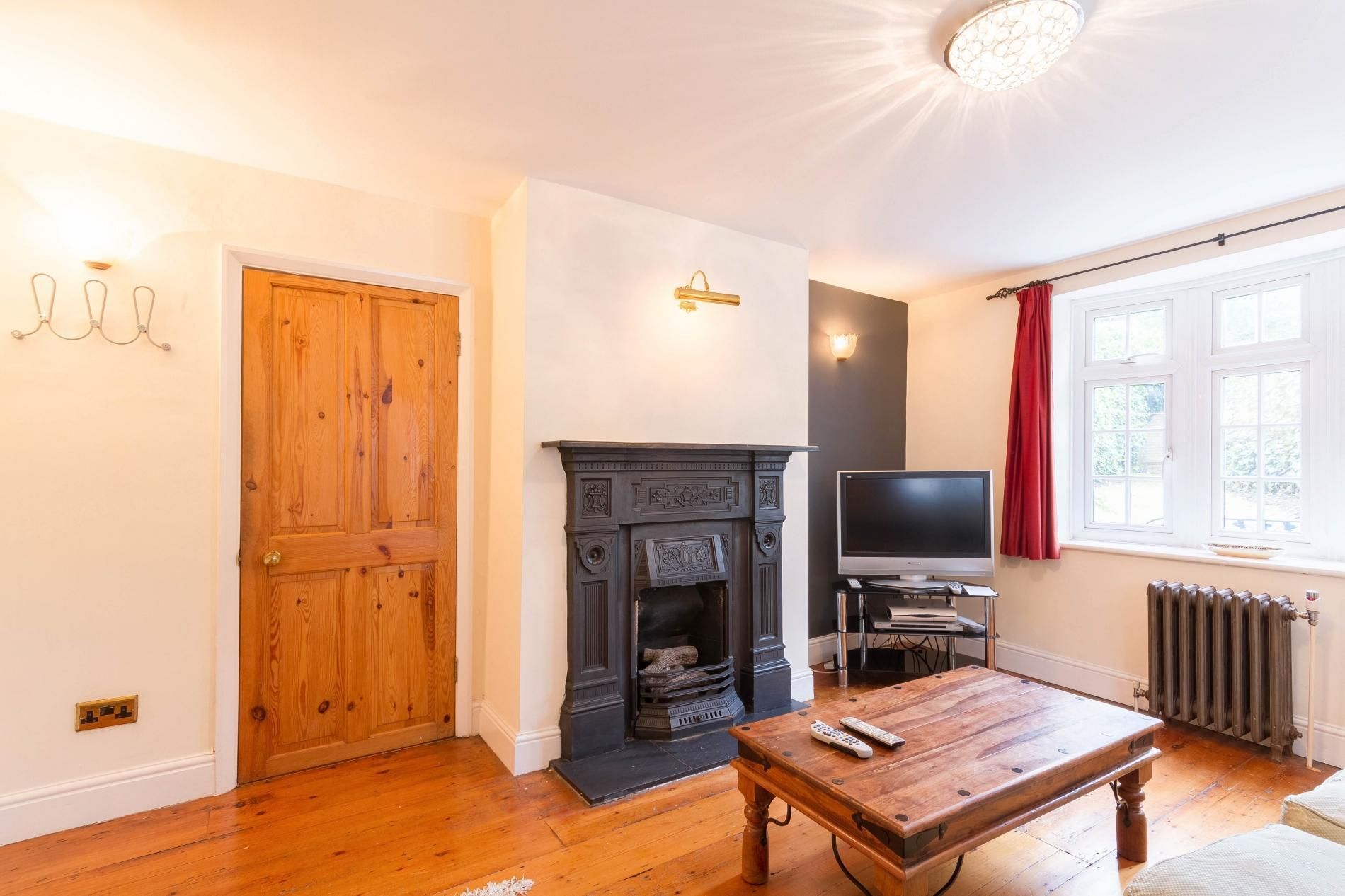 A room with a wooden door, a fireplace, a television, and a window with curtains.