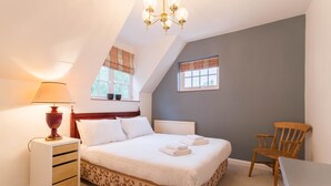 Un dormitorio con cama, mesita de noche con lámpara, una silla y una ventana con cortinas.