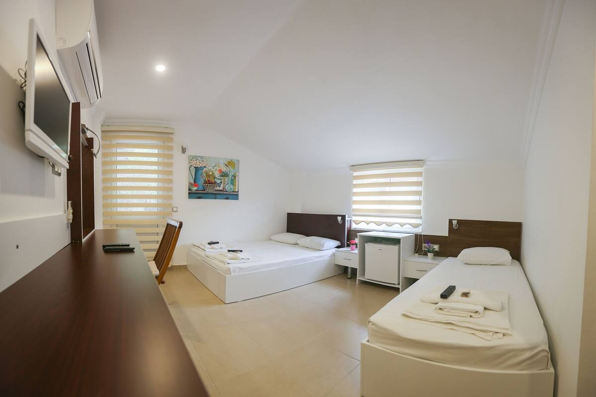Een kleine hotelkamer met een bed, een bureau, een stoel, een televisie en een schilderij aan de muur.