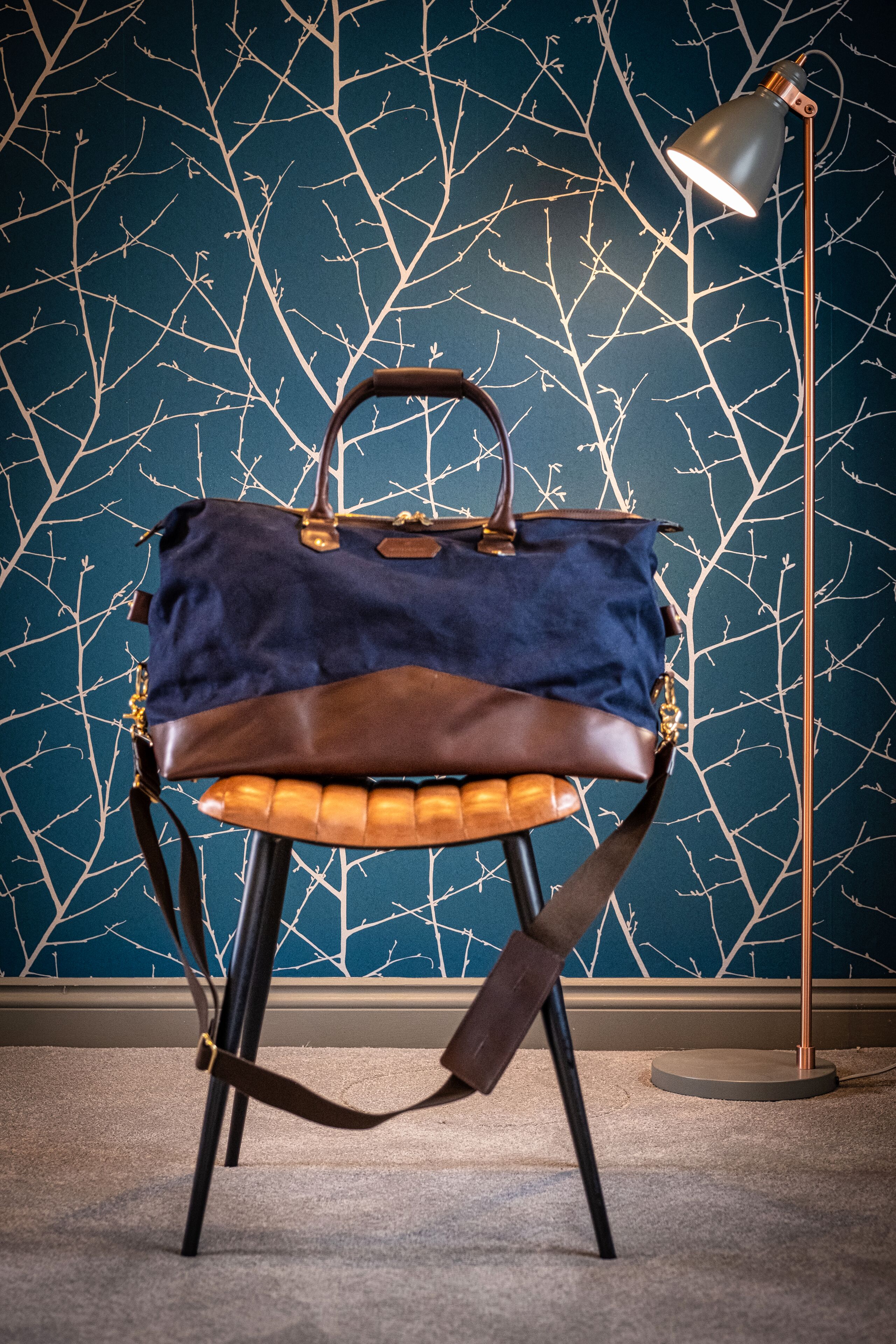 Una silla con un bolso encima, una lámpara de pie y una pared con un diseño de rama de árbol.