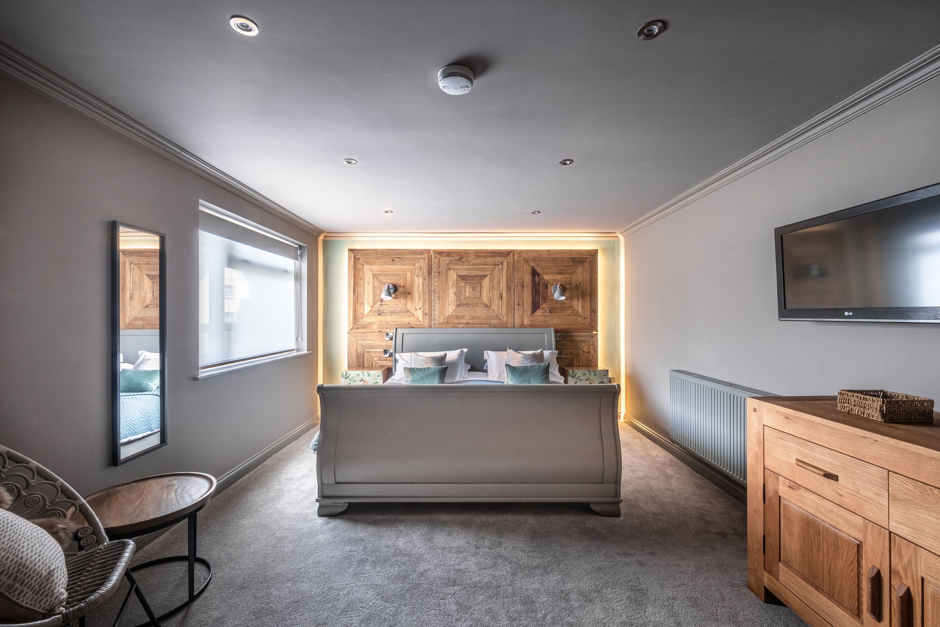 A bedroom with a bed, a wooden headboard, a TV mounted on the wall, a wooden cabinet, and a chair.