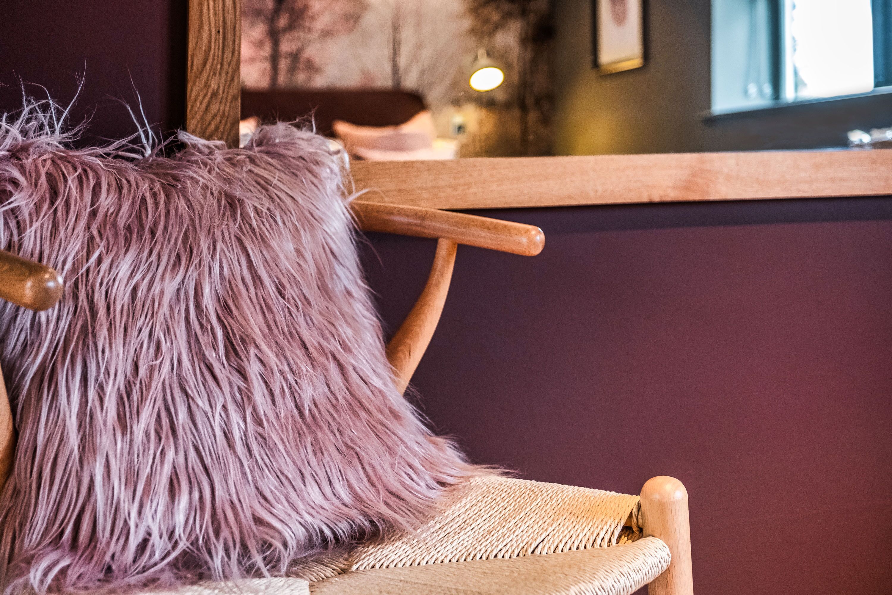 A wooden chair with a woven seat and a fluffy, textured pillow.