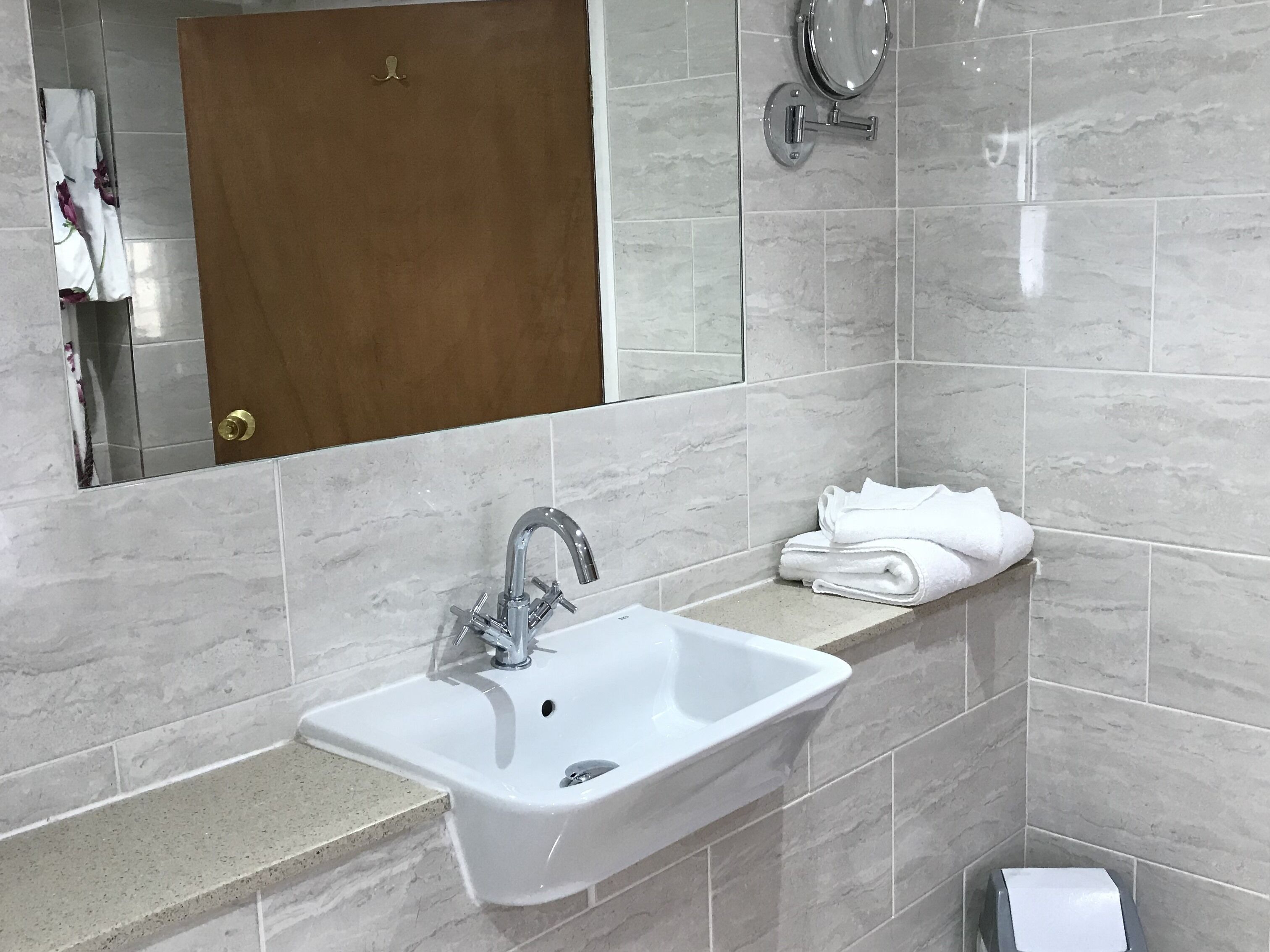 Un baño con un lavamanos blanco, un espejo y un perchero para toallas.