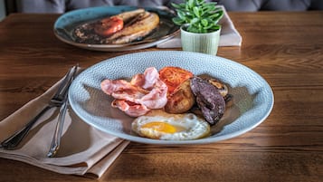 Prato de café da manhã com ovos, bacon, tomates e linguiça em mesa de madeira.