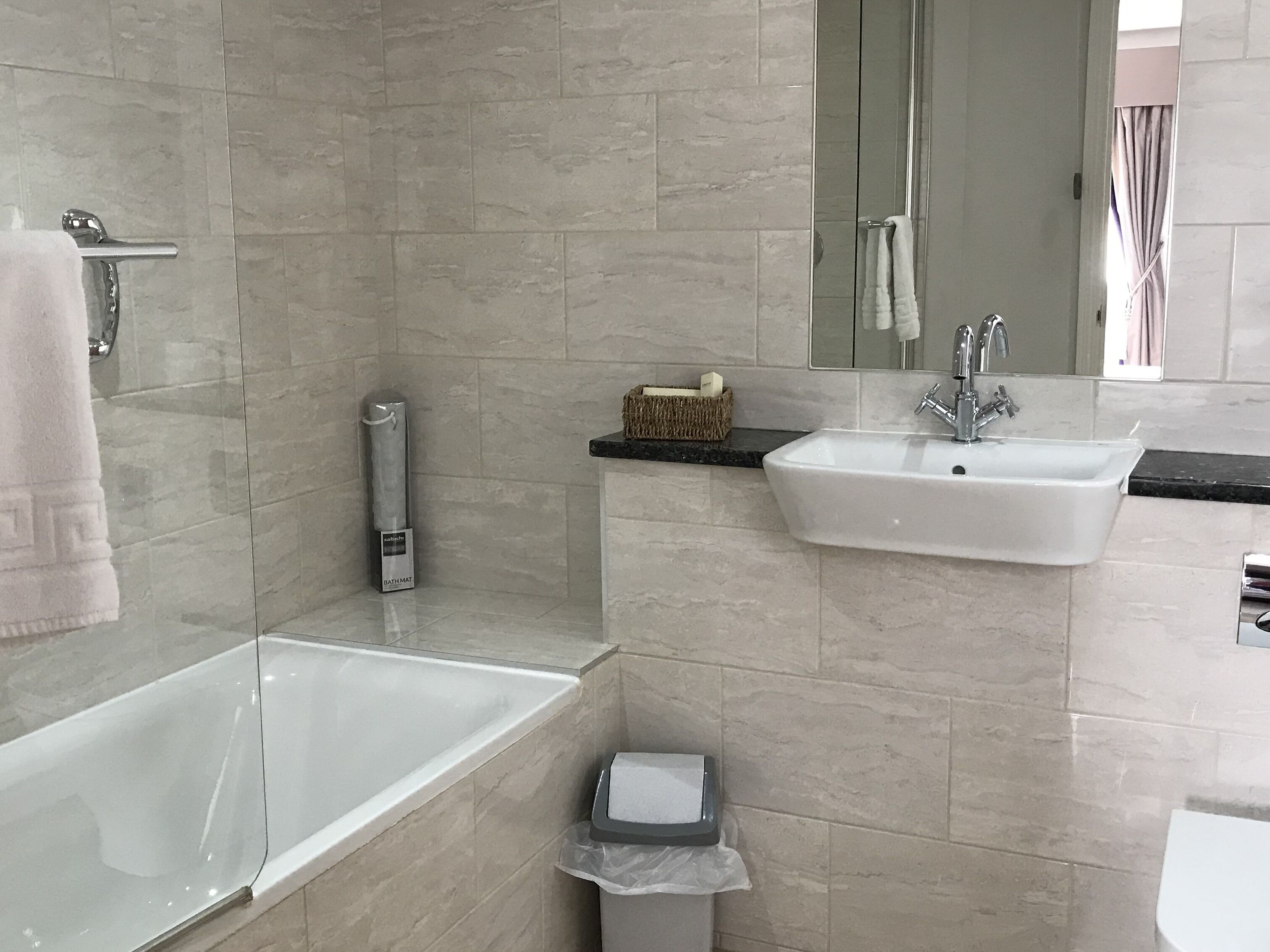 A modern bathroom with a glass bathtub, a white sink, and a mirror above the sink.
