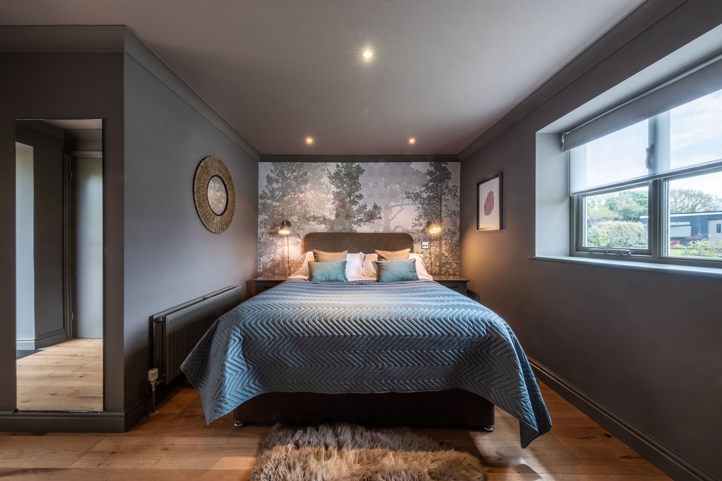 A modern bedroom with a large bed, a view of the outdoors through a window, and a unique wall art piece.