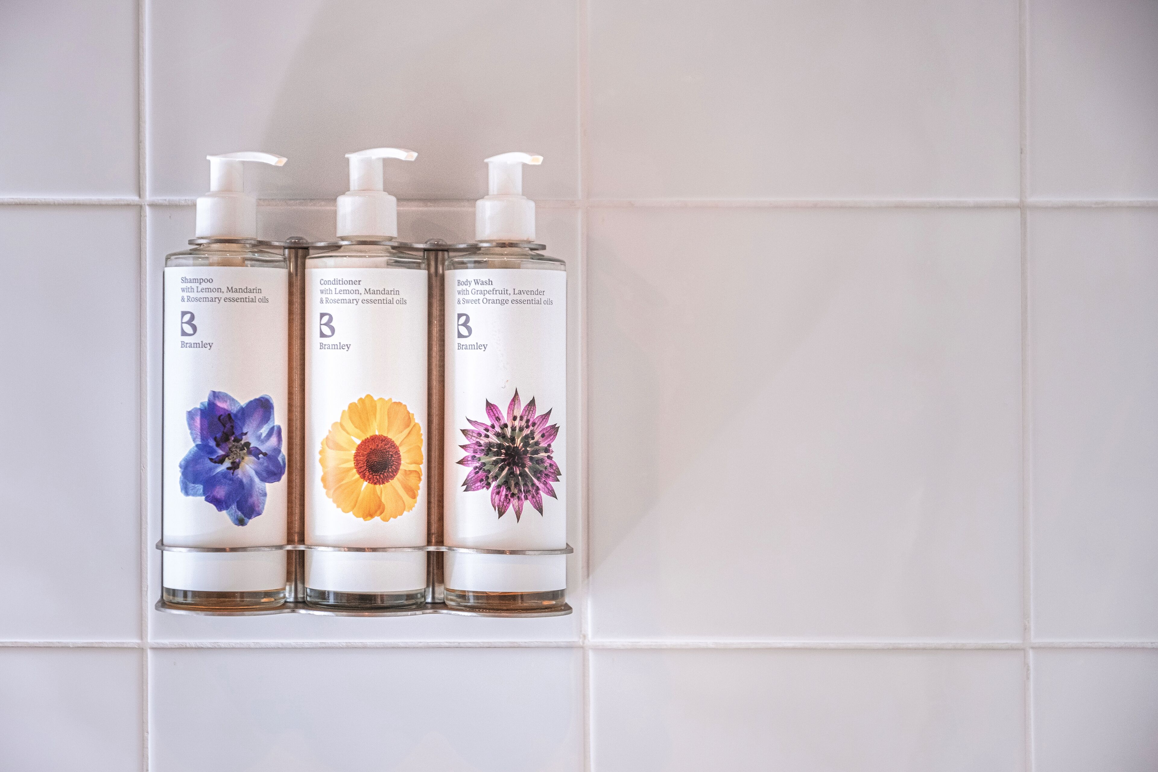 Tre flaconi di bagnoschiuma e balsamo Bramley con diverse illustrazioni floreali.