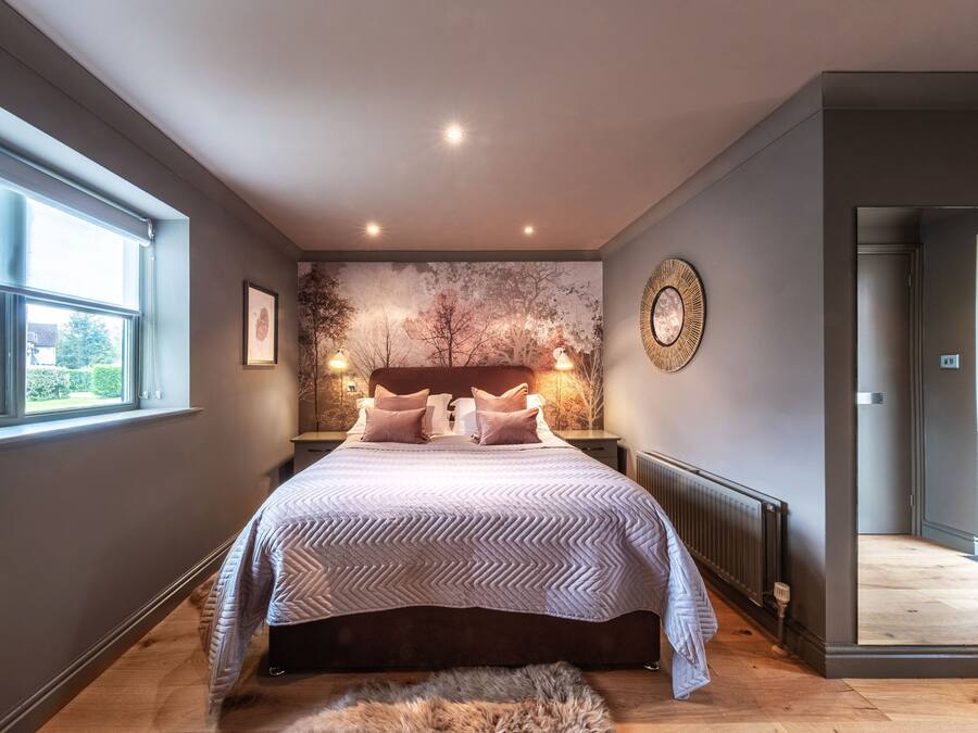 A bedroom with a large bed, a window, a wall-mounted artwork, and a mirror.