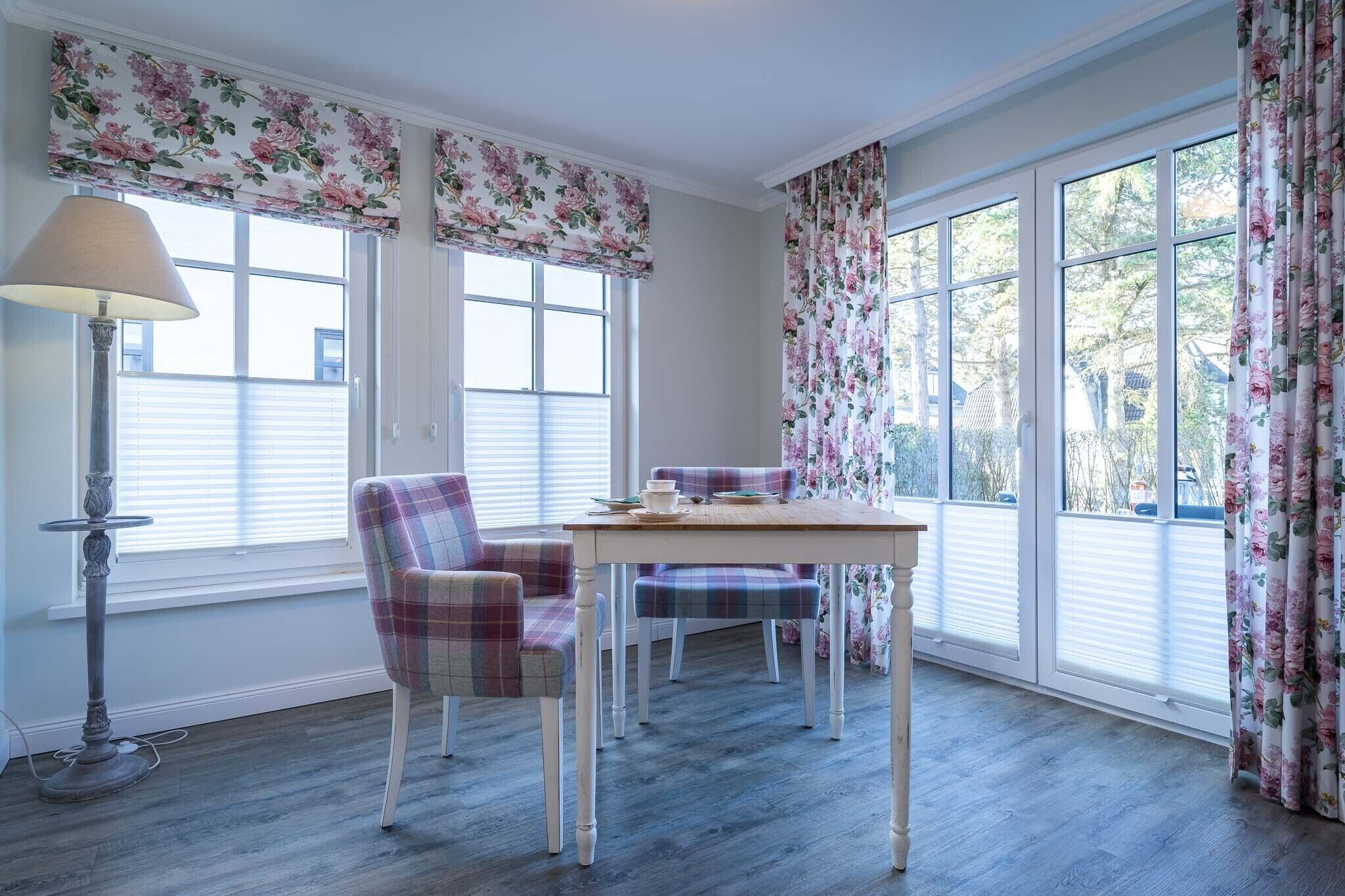 Un espace repas comprenant une table et des chaises, de grandes fenêtres équipées de stores et un lampadaire.