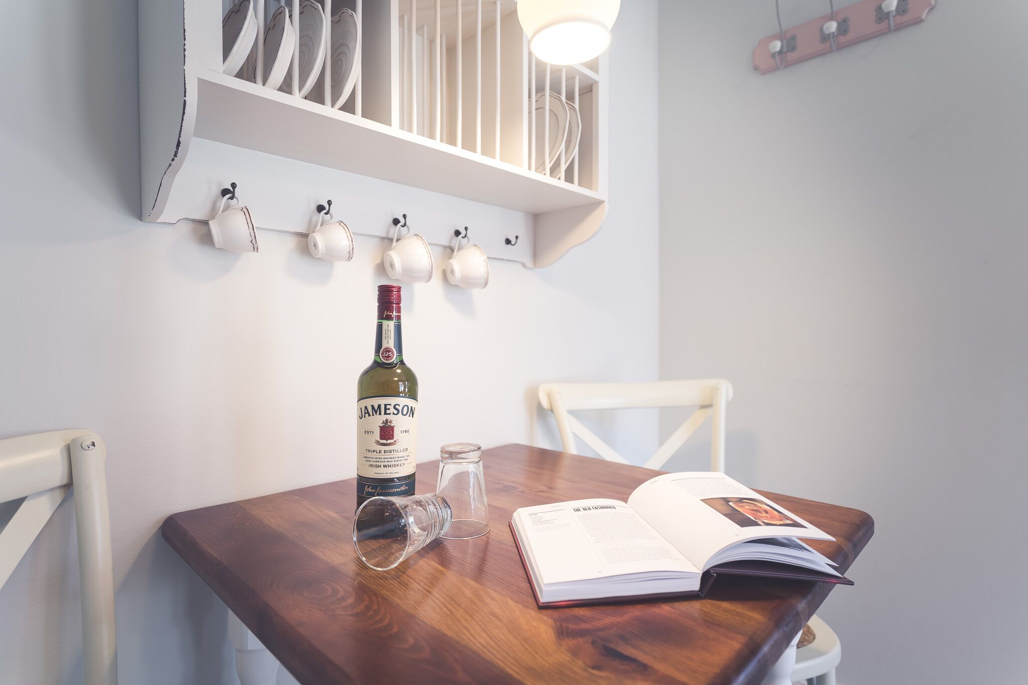 Ein Holztisch mit einer Jameson Whiskey-Flasche, einem Glas und einem offenen Buch.