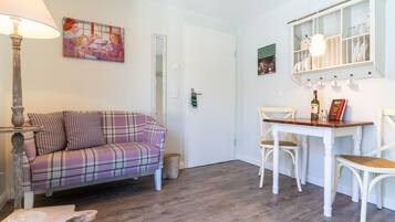A cozy living room with a plaid sofa, a dining table with chairs, a lamp, and a wall-mounted cabinet with dishes.