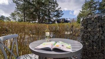 A round metal table with an open magazine, a bottle of wine, and two glasses.