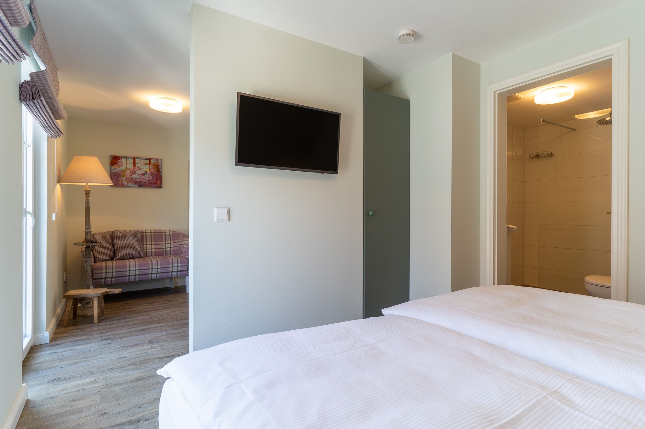 Une chambre d’hôtel avec un lit, un téléviseur fixé au mur, un canapé et une petite table.