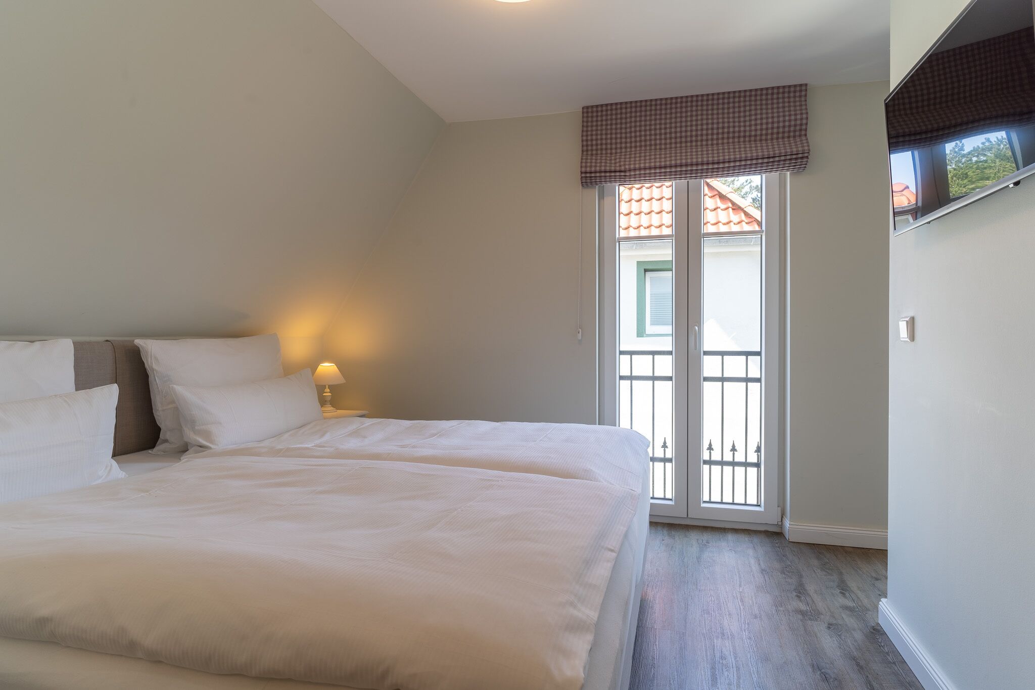 A bedroom with a large bed, a nightstand with a lamp, and a window with a view of a building.