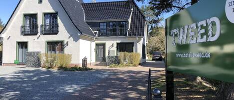 A two-story house with a sloped roof, a balcony, and a gravel driveway.