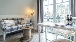 A cozy room with a plaid sofa, a round wooden table, and a view through large windows. - Hotel Tweed (St. Peter-Ording)