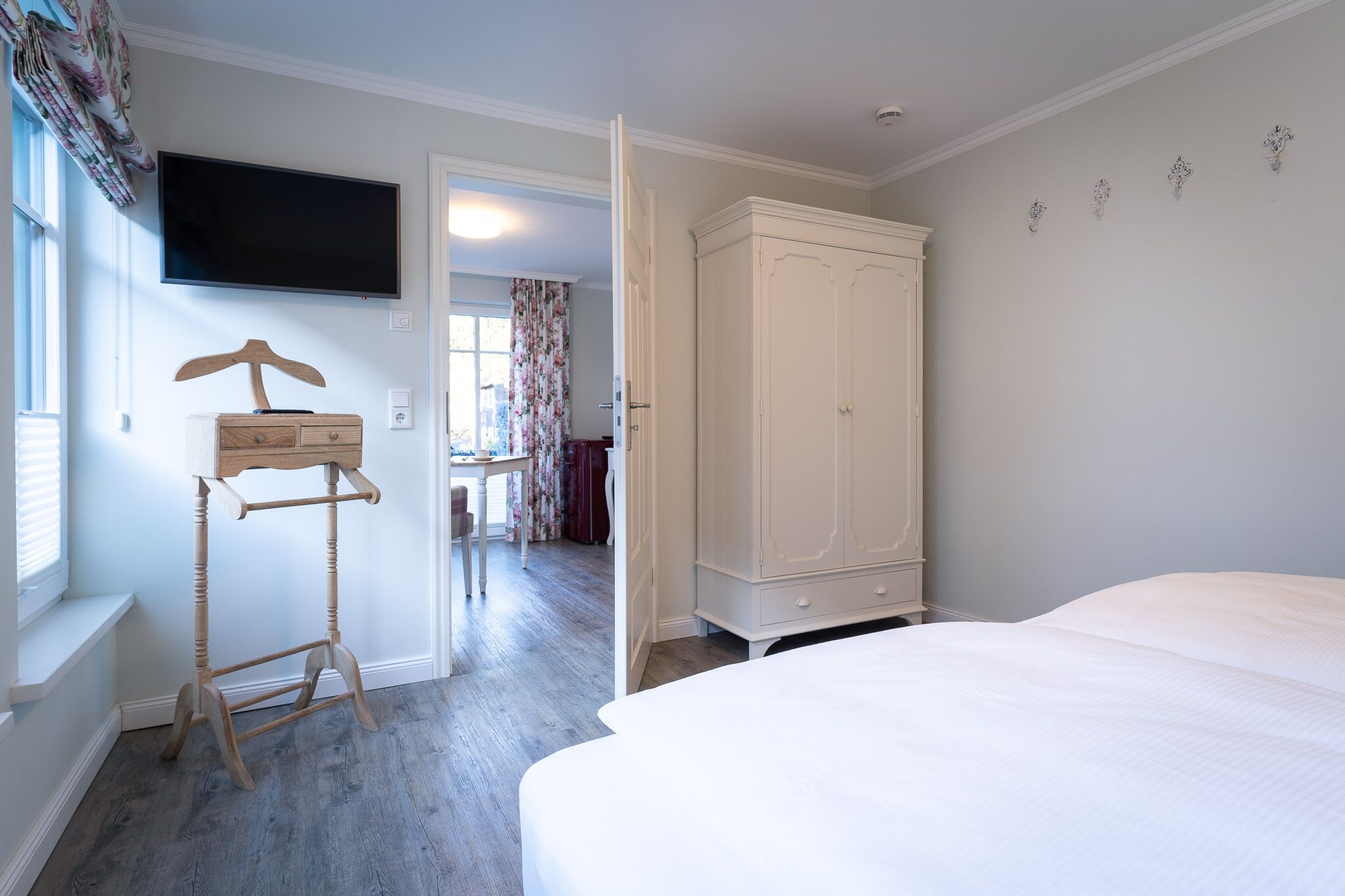 A bedroom with a bed, a wardrobe, a TV mounted on the wall, and a wooden hanger stand.