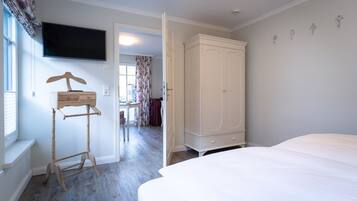 A bedroom with a bed, a wardrobe, a TV mounted on the wall, and a wooden hanger stand.