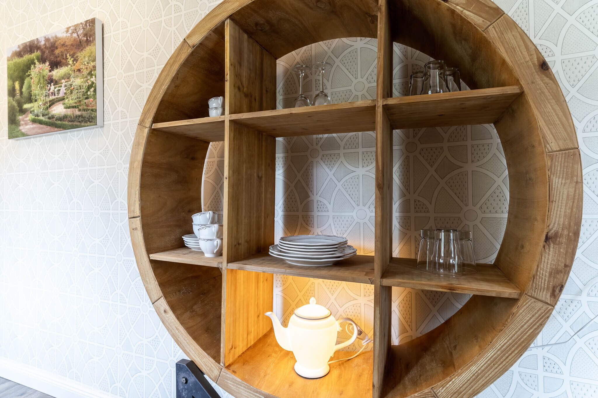 Ein rundes Regal aus Holz mit Fächern, die Teller, Tassen, Gläser und einen Teekessel enthalten.