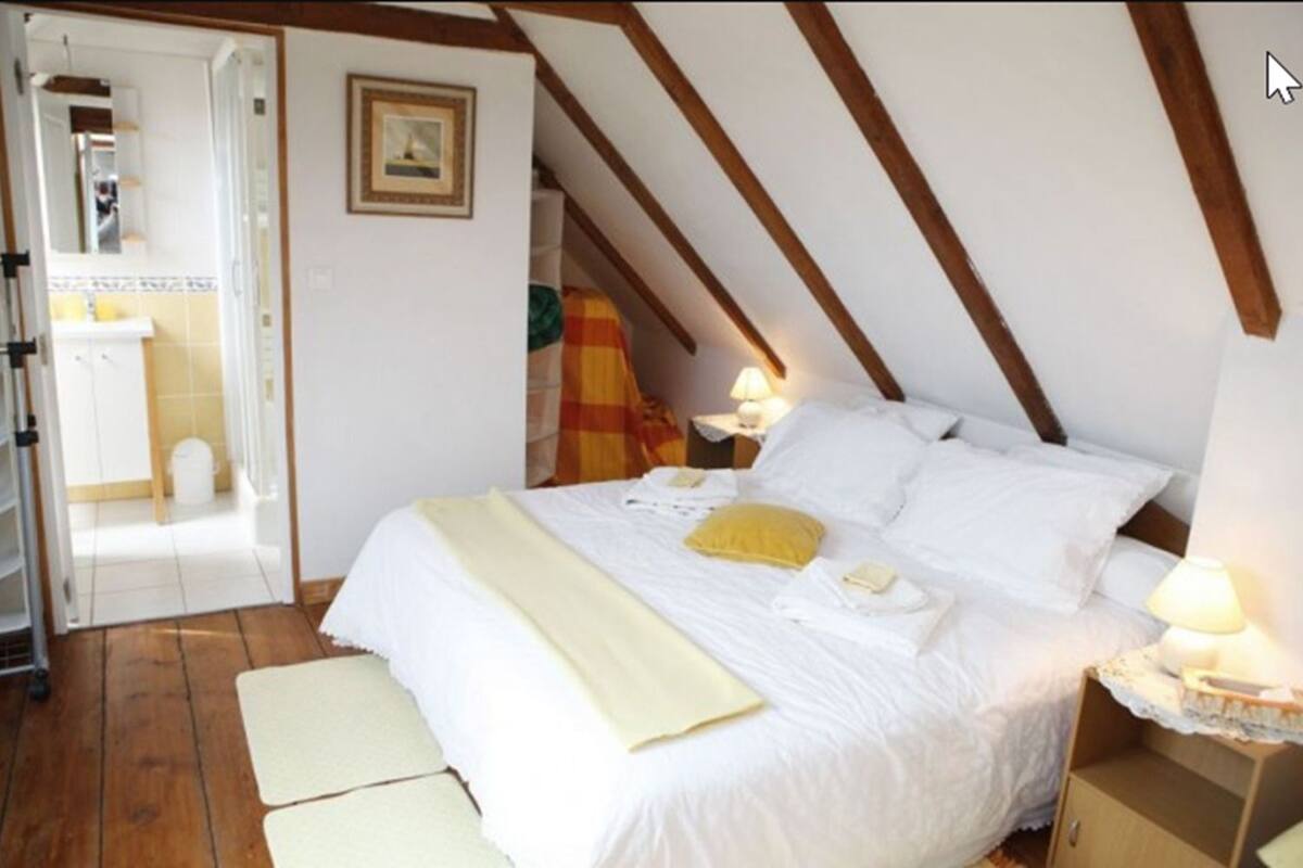 A bedroom with a bed, bedside tables, a nightstand, a window, and a door leading to a bathroom.